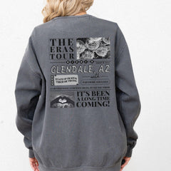 a woman wearing a gray sweatshirt with a tour poster on it