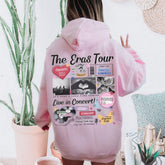 a woman wearing a pink hoodie with the words the eras tour on it