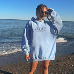 a woman standing on a beach wearing a blue hoodie