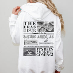 a woman wearing a white hoodie with the words the eras tour on it