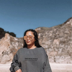 a woman wearing a sweatshirt and glasses standing in front of a mountain