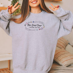 a woman wearing a grey sweatshirt with the words the east tour written on it