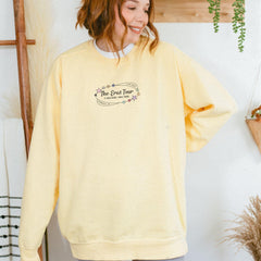 a woman standing in front of a wall wearing a yellow sweatshirt