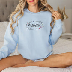 a woman sitting on a bed wearing a blue sweatshirt