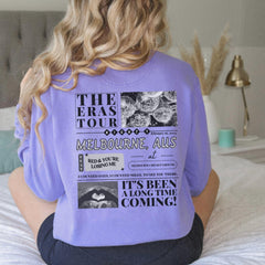 a woman sitting on a bed wearing a purple shirt