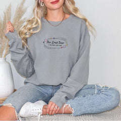 a woman sitting on a bed wearing a grey sweatshirt