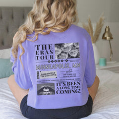 a woman sitting on a bed wearing a purple shirt