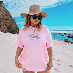 a woman standing on a beach wearing a pink shirt and hat