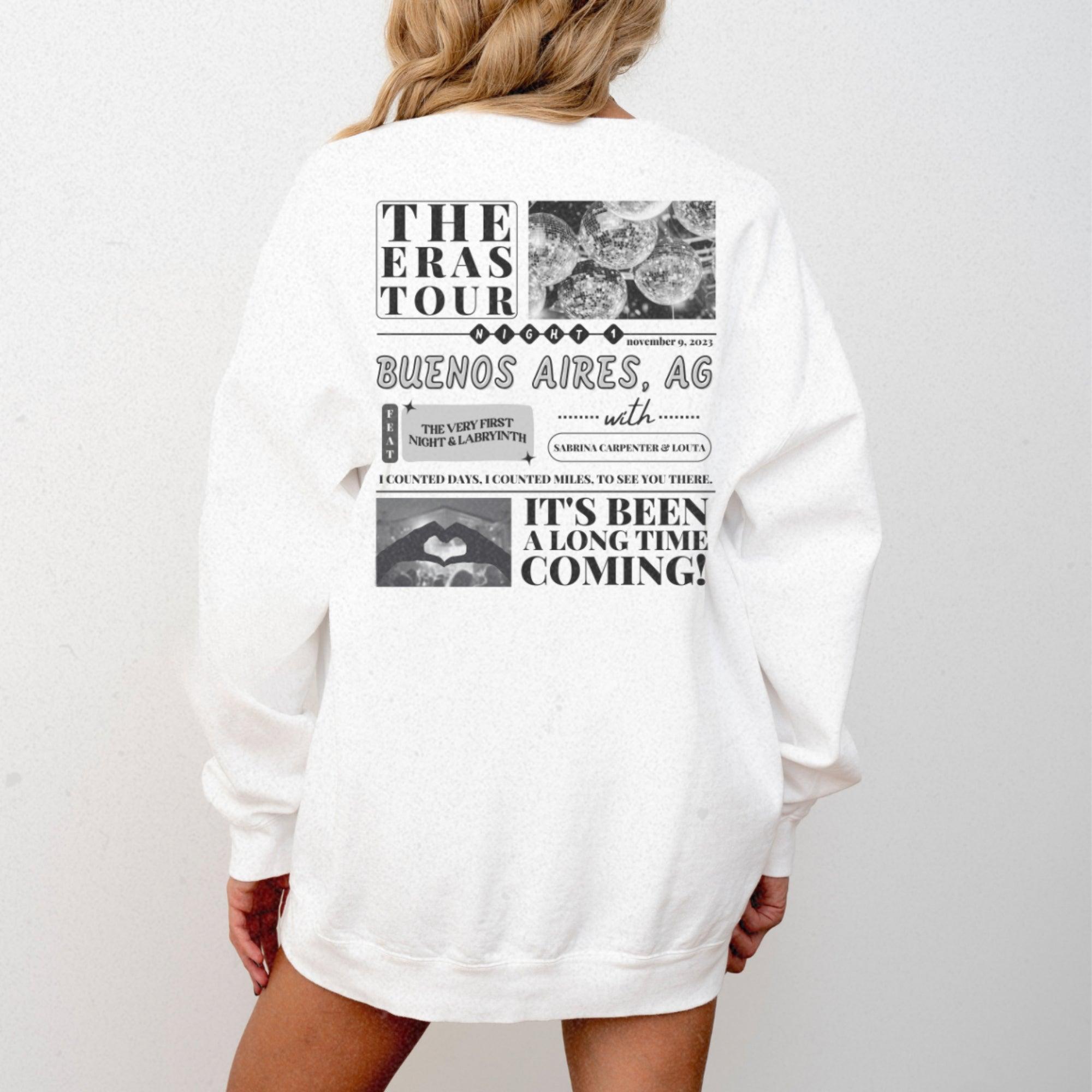 a woman wearing a white sweatshirt with the words the eras tour on it