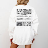 a woman wearing a white sweatshirt with the words the eras tour on it