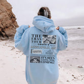 a person standing on a beach wearing a blue hoodie