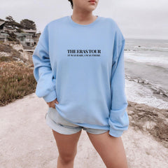 a woman standing on a beach wearing a blue sweatshirt