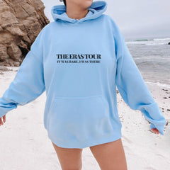 a woman standing on a beach wearing a blue sweatshirt