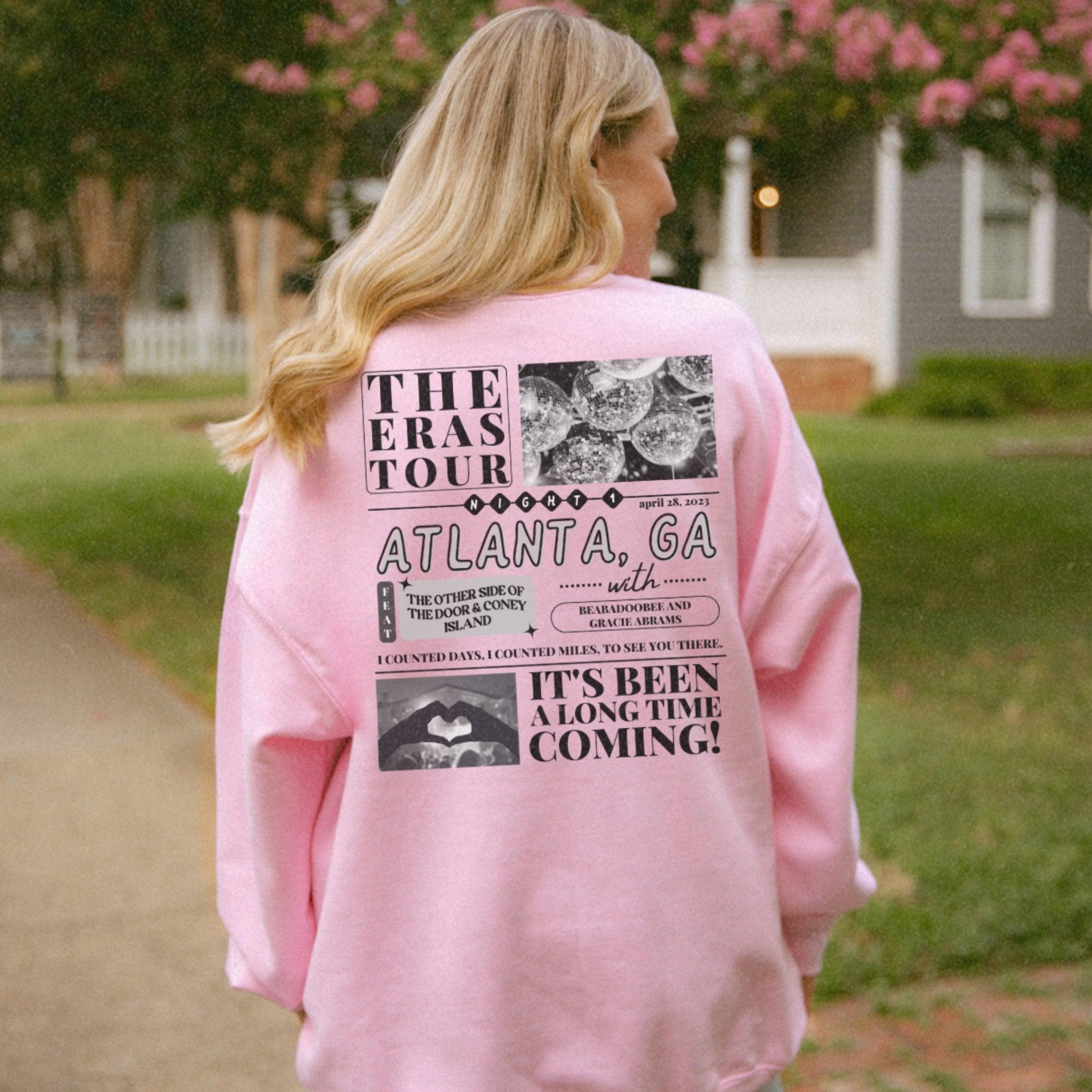 a woman in a pink sweatshirt is standing on a sidewalk