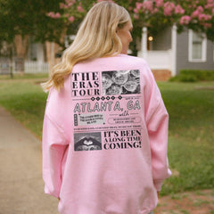 a woman in a pink sweatshirt is standing on a sidewalk