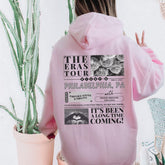 a woman wearing a pink hoodie with the words the eras tour philadelphia pa on