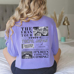 a woman sitting on a bed wearing a purple shirt