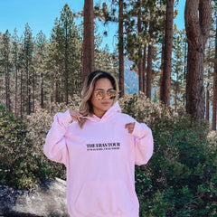 a woman in a pink hoodie is standing in the woods