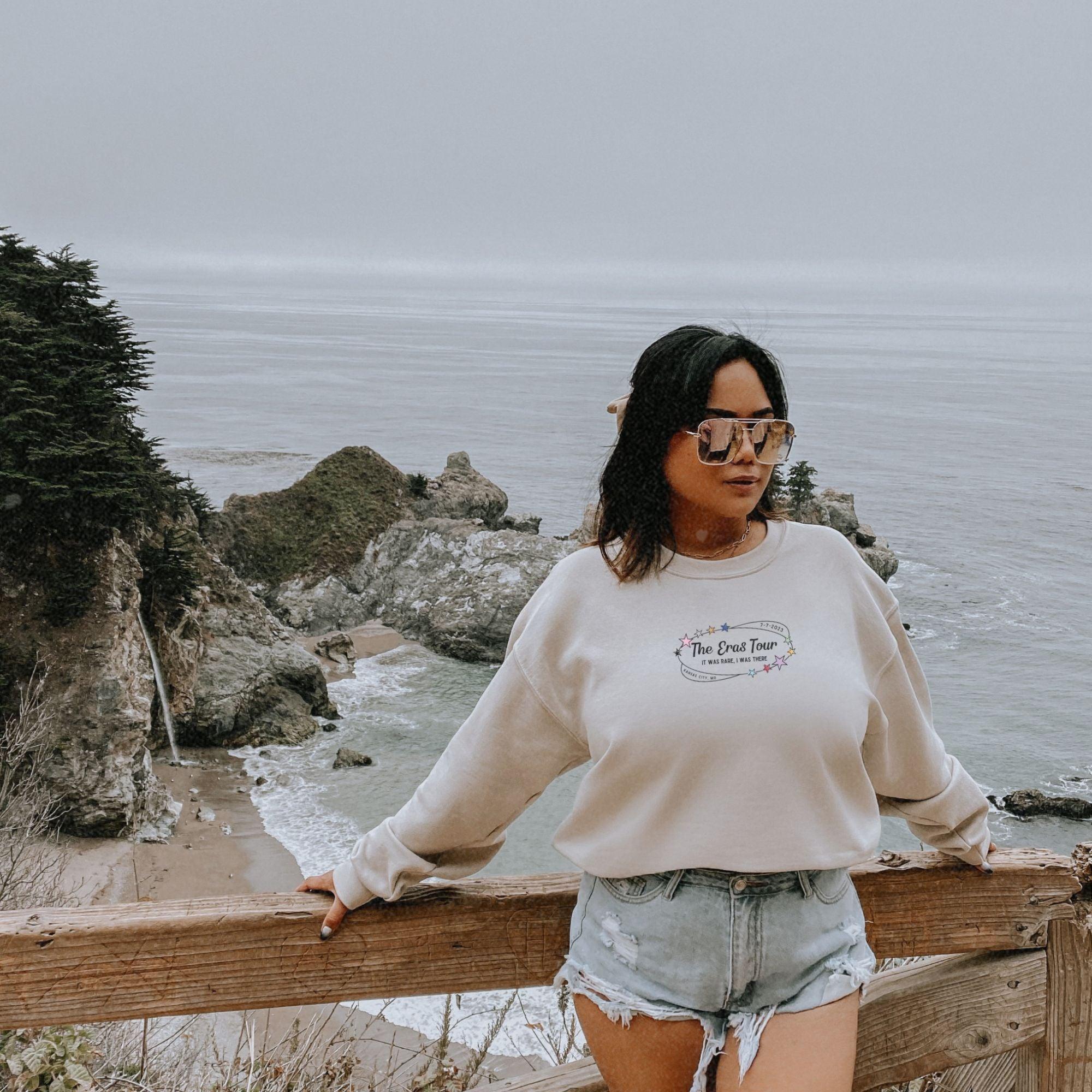 a woman standing on top of a wooden fence next to the ocean
