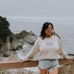 a woman standing on top of a wooden fence next to the ocean