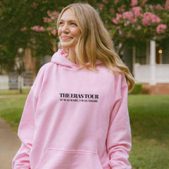 a woman in a pink hoodie smiles while standing on a sidewalk
