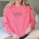 a woman sitting on a bed wearing a pink sweatshirt
