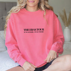 a woman sitting on a bed wearing a pink sweatshirt