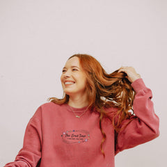 a woman with red hair wearing a pink sweatshirt