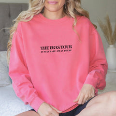 a woman sitting on a bed wearing a pink sweatshirt