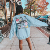 a woman in a blue sweatshirt is walking down the sidewalk