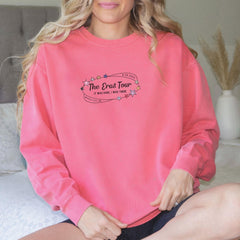 a woman sitting on a bed wearing a pink sweatshirt