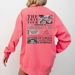 a woman wearing a pink sweatshirt with the words the eras tour on it