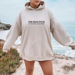 a woman standing on a beach wearing a hoodie