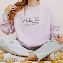 a woman sitting on a bed wearing a purple sweatshirt