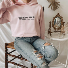 a woman sitting on a chair wearing a pink sweatshirt