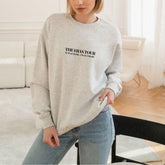 a woman standing in a living room wearing a grey sweatshirt