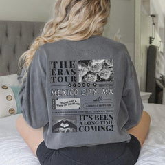 a woman sitting on a bed wearing a gray shirt