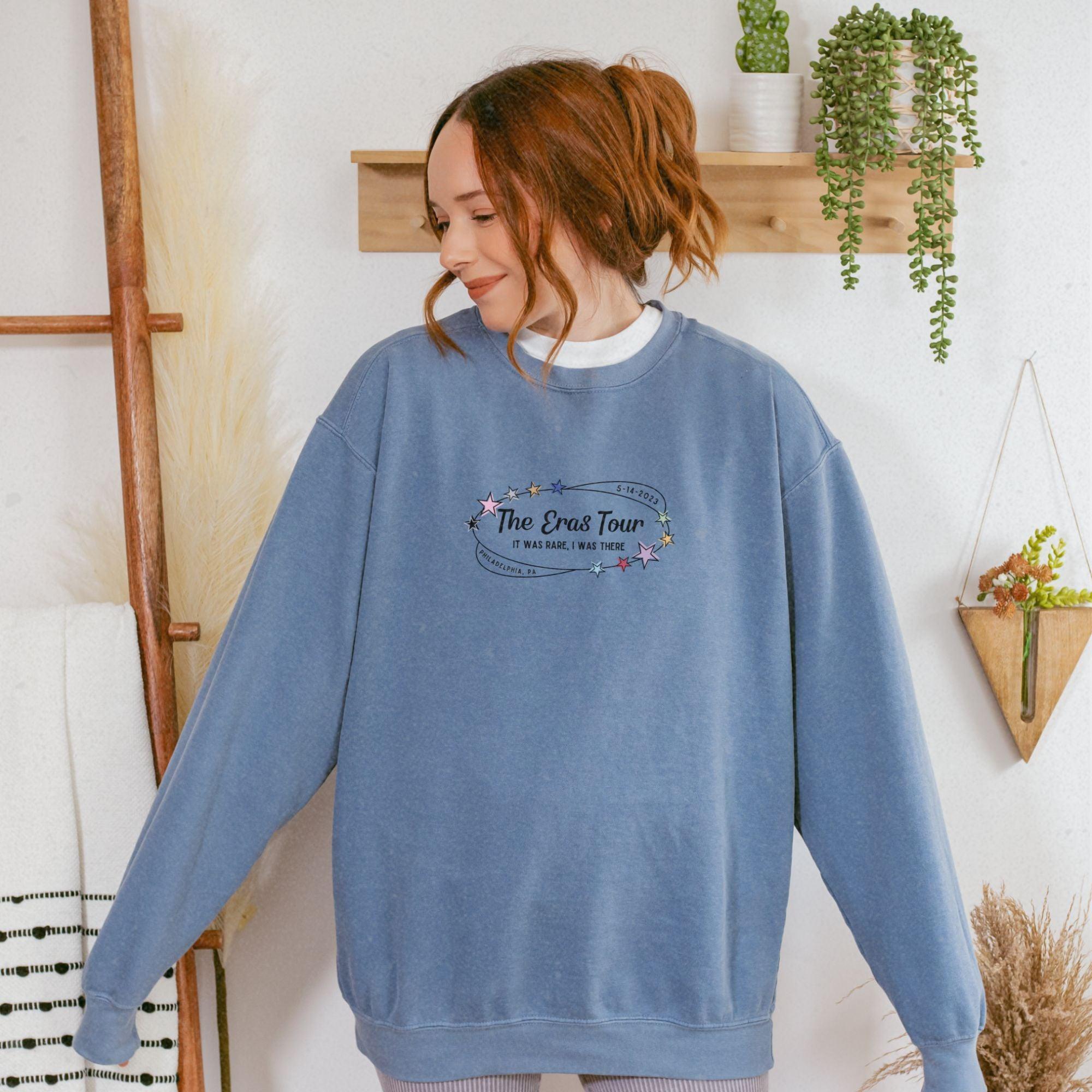 a woman standing in front of a wall wearing a blue sweatshirt