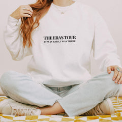a woman sitting on a bed wearing a white sweatshirt