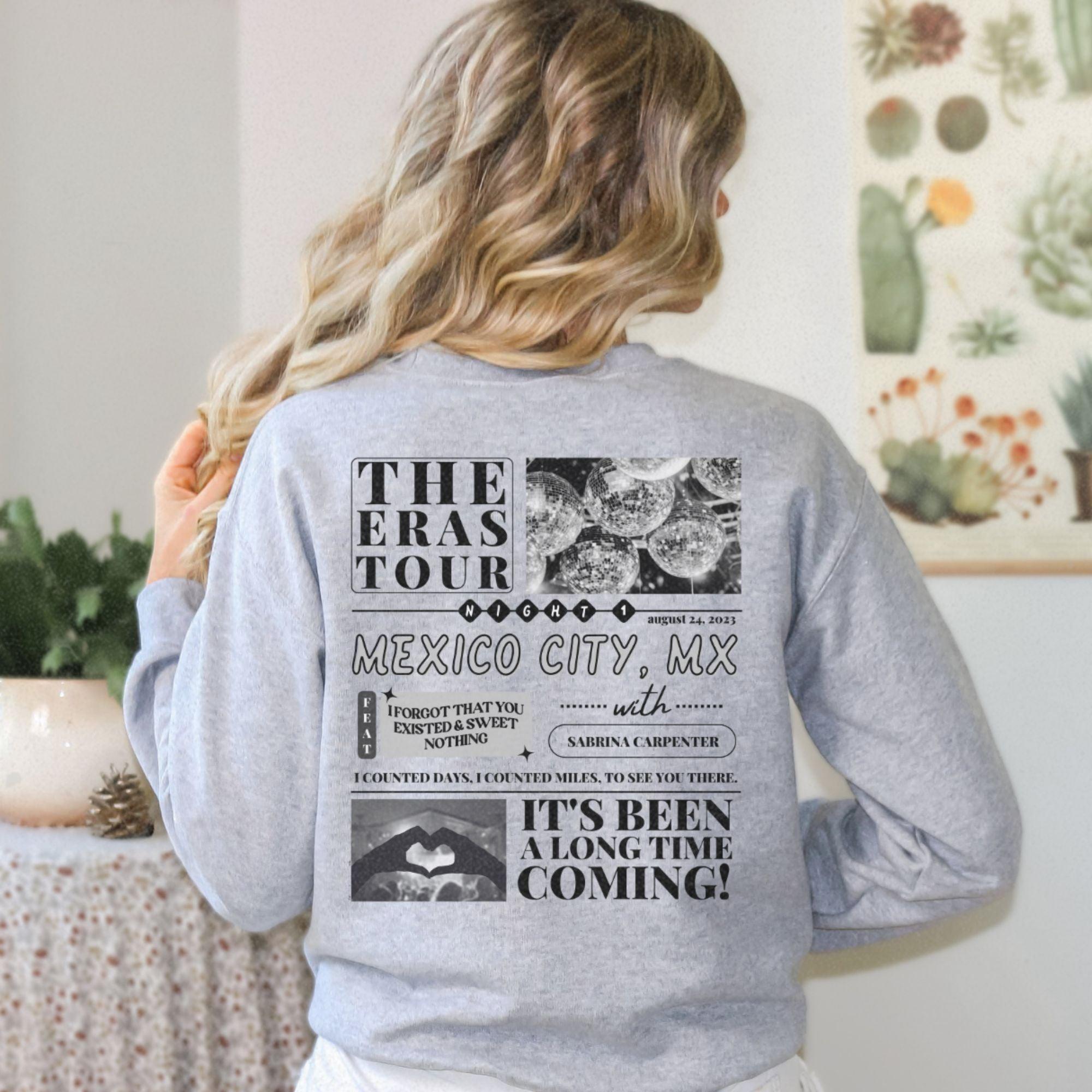 a woman standing in front of a wall wearing a sweatshirt