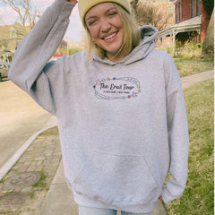 a woman in a gray hoodie smiles while standing on a sidewalk