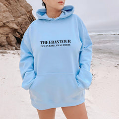 a woman standing on a beach wearing a blue hoodie