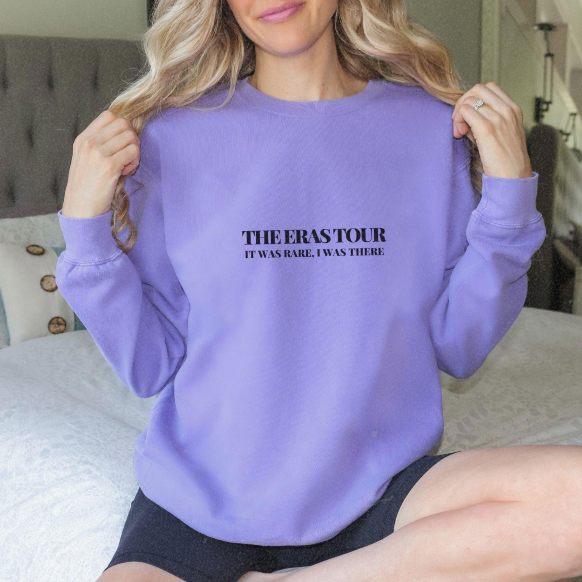 a woman sitting on a bed wearing a purple sweatshirt