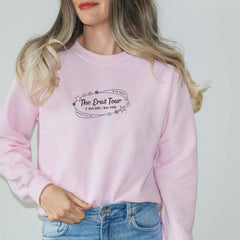 a woman wearing a pink sweatshirt with the words the best tour on it