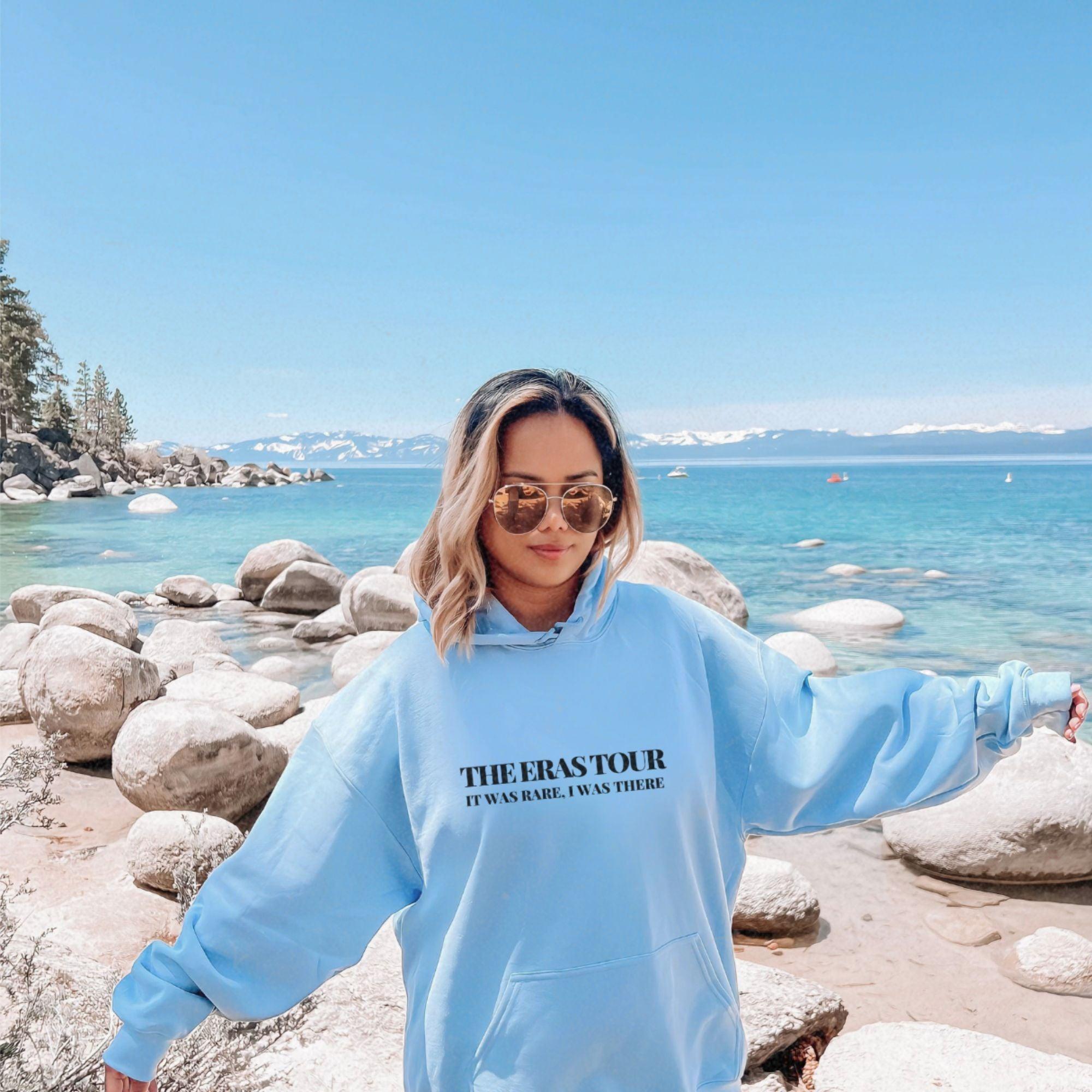 a woman in a blue sweatshirt standing on a rocky beach