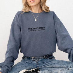 a woman sitting on the ground wearing a sweatshirt