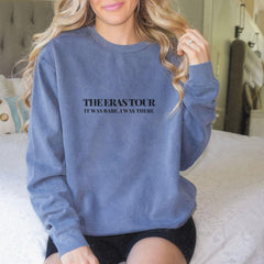 a woman sitting on a bed wearing a sweatshirt