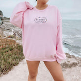 a woman in a pink sweatshirt standing on a beach