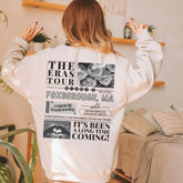 a woman wearing a white sweatshirt with the words the eras tour on it