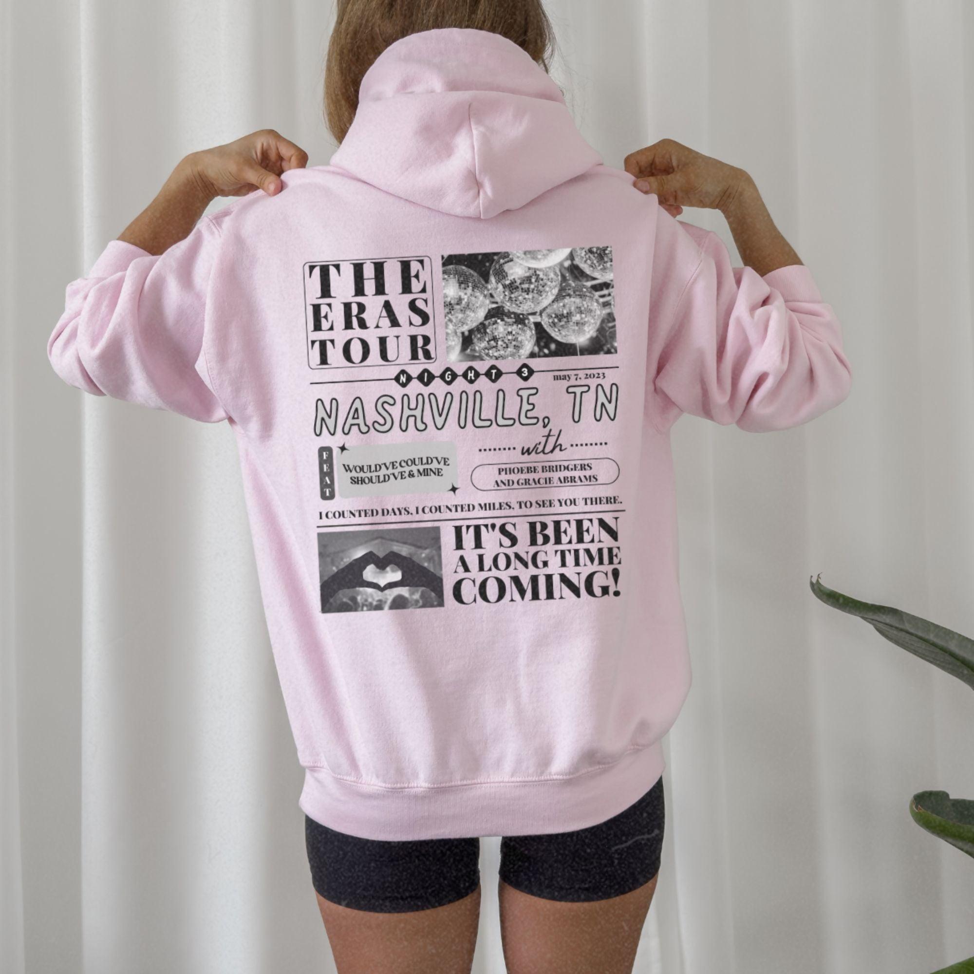 a woman wearing a pink hoodie with the words the eras tour nashville on it